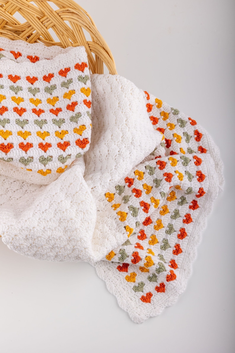 crochet baby heart blanket pattern with white yarn as base color in the middle with the shell stitch and autumn colors green orange and red for the hearts