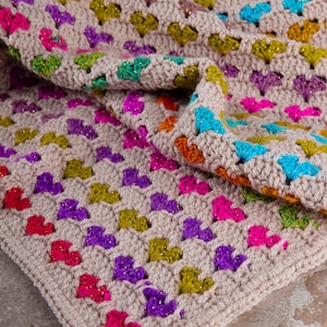 close up photo of the crochet heart blanket pattern with hearts in rainbow colors made with variegated yarn and beige yarn as the base color of the blanket.