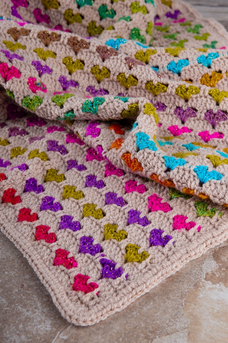 close up photo of the crochet heart blanket pattern with hearts in rainbow colors made with variegated yarn and beige yarn as the base color of the blanket.