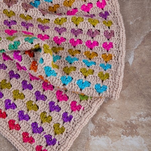 close up photo of the crochet heart blanket pattern with hearts in rainbow colors made with variegated yarn and beige yarn as the base color of the blanket.