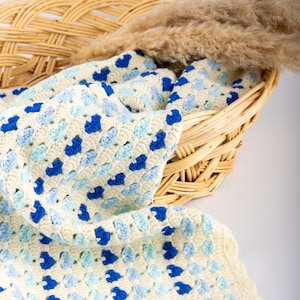 crochet heart blanket pattern made with yarn in shades of blue for the hearts and white as the base of the afghan. Shown folded in a woven basket.