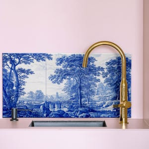 May include: A gold kitchen faucet with a high arc spout and a lever handle. The faucet is mounted on a pink tiled backsplash with a blue and white patterned design.