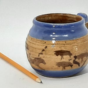 May include: A blue and brown ceramic mug with a handle. The mug features a design of brown animals on a tan background.