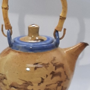 May include: A ceramic teapot with a bamboo handle. The teapot is decorated with a brown and white pattern of running horses. The teapot has a blue and gold lid.