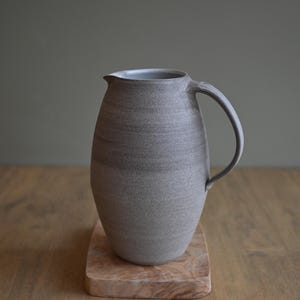 May include: A grey ceramic jug with a textured surface and a rounded body. The jug has a handle and a spout.
