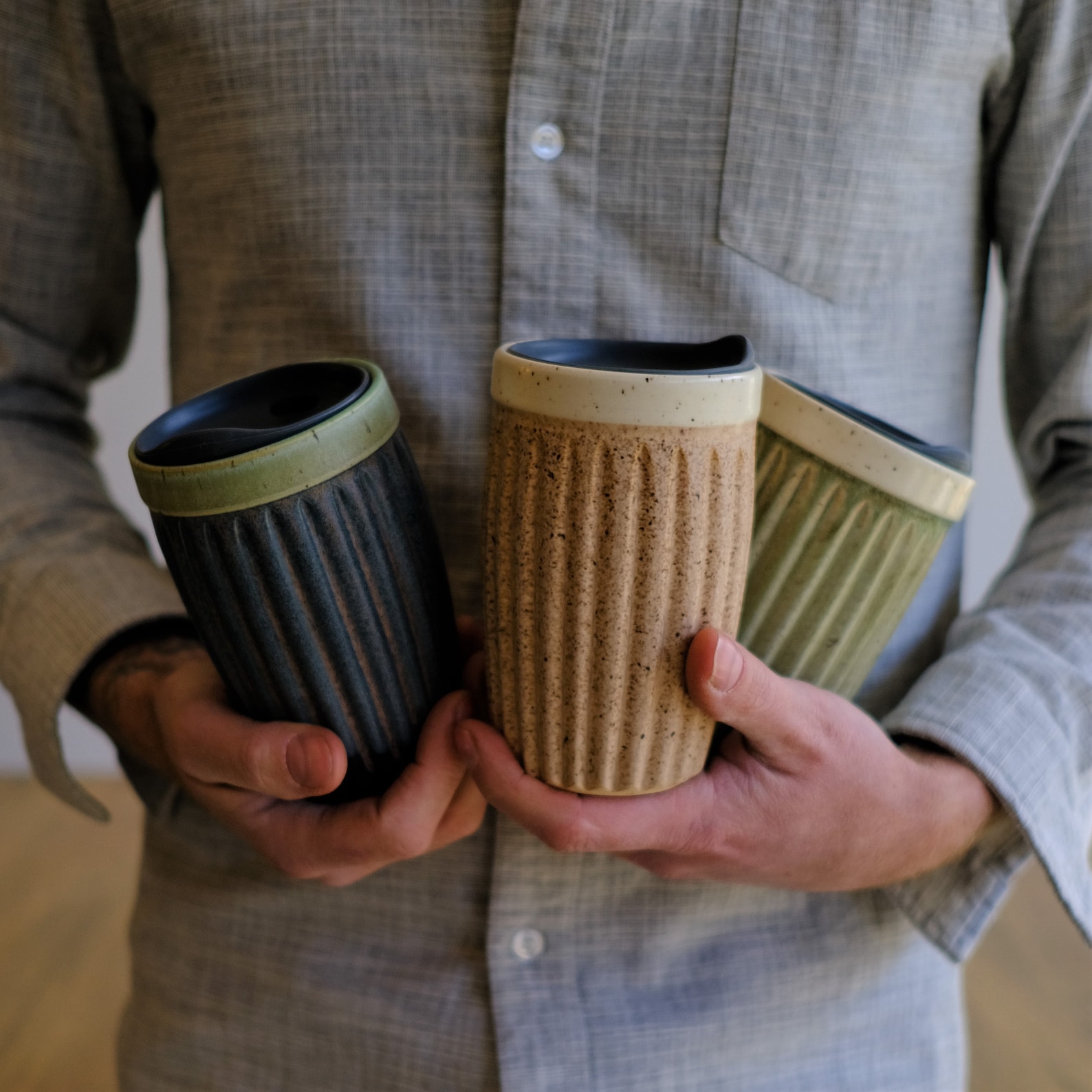 A collection of three ceramic travel mugs being held in a man's arms