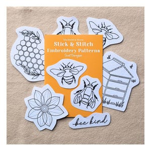 May include: A set of white stick and stitch embroidery patterns with black line art designs including bees, a honeycomb, a flower, a beehive, and the text "bee kind" arranged around an orange card labelled "blackbird & bloom Stick & Stitch Embroidery Patterns Sweet Honeybee."
