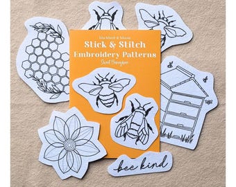 May include: A set of white stick and stitch embroidery patterns with black line art designs including bees, a honeycomb, a flower, a beehive, and the text "bee kind" arranged around an orange card labelled "blackbird & bloom Stick & Stitch Embroidery Patterns Sweet Honeybee."