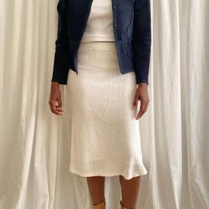 K&ouml;nnte beinhalten: Marineblaue Wildlederjacke mit floralen Applikationen und wei&szlig;em, strukturiertem Rock. Die Jacke hat einen runden Ausschnitt und lange &Auml;rmel. Der Rock ist knielang und das Model tr&auml;gt braune Stiefel.