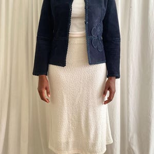 K&ouml;nnte beinhalten: Marineblaue Wildlederjacke mit floraler Applikation, kombiniert mit einem wei&szlig;en Rock. Die Jacke hat einen runden Ausschnitt und dekorative N&auml;hte. Der Rock ist ein strukturierter, knielanger Stil.
