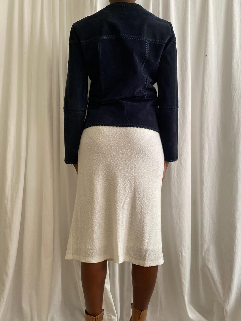 K&ouml;nnte beinhalten: Marineblaue Wildlederjacke mit sichtbaren Steppn&auml;hten, kombiniert mit einem wei&szlig;en, strukturierten knielangen Rock. Die Jacke hat lange &Auml;rmel und eine taillierte Passform. Der Rock hat eine leichte A-Linien-Form.