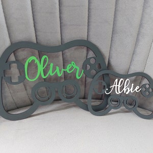 May include: Two black wooden game controller shapes with the names "Oliver" in green and "Albie" in white.