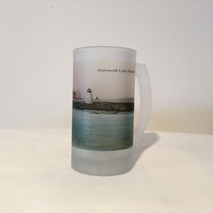 May include: A frosted glass beer stein with a picture of the Straitsmouth Light lighthouse in Rockport, Massachusetts. The image shows the lighthouse on a rocky outcropping with the ocean in the background.