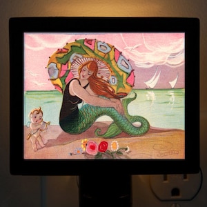 Może przedstawiać: Winietkowa pocztówka przedstawiająca syrenę w kolorowym, wzorzystym kapeluszu, siedzącą na plaży z małą figurką cherubina. Syrena ma zielony ogon i nosi czarny kostium kąpielowy. Na pocztówce widnieje różowe i niebieskie niebo z białymi chmurami i żaglówkami w oddali.