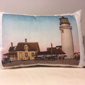 Może przedstawiać: Biała poduszka z obrazem vintage pocztówki przedstawiającej latarnię morską, dom i powóz ciągnięty przez konie. Na pocztówce widnieje napis "Highland Light, North Truro, Mass."