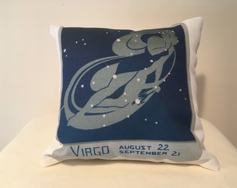 May include: A white pillow with a blue background featuring a stylized image of the Virgo constellation. The text "VIRGO AUGUST 22 SEPTEMBER 21" is printed on the pillow.