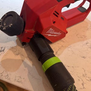 Puede incluir: Una herramienta eléctrica roja Milwaukee con un dial negro ajustable y un accesorio de manguera negro y verde. La herramienta tiene el logotipo de Milwaukee en el lateral.