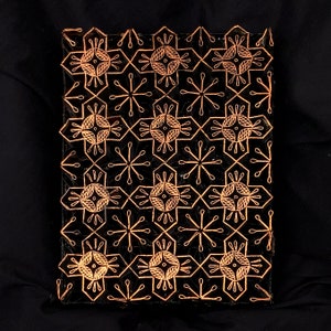 May include: A black and gold wooden block with a repeating geometric pattern. The pattern is made up of small circles and lines.