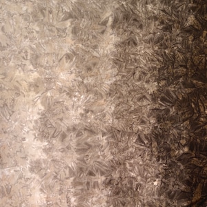 May include: A close-up of a textured surface with a gradient of light brown to dark brown. The surface has a pattern of small, irregular shapes that resemble crystals.