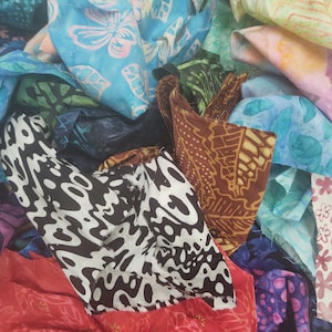 May include: A pile of colorful fabric scraps with various patterns, including floral, geometric, and abstract designs. The fabrics are in shades of blue, green, brown, pink, white, and black.