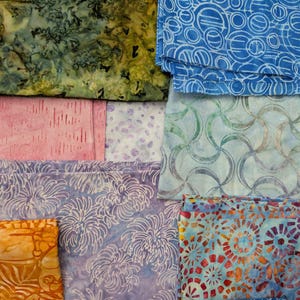 May include: A collection of folded fabric pieces featuring various patterns and colors, including a green mottled print, a blue geometric circle design, a pink textured pattern, a light blue wave motif, a purple floral print, and an orange leaf design.