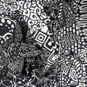 May include: Close-up of a collection of fabric pieces with various black and white geometric patterns. The patterns include swirls, dots, squares, and other abstract shapes. The fabric is bunched together, creating a textured and layered appearance.