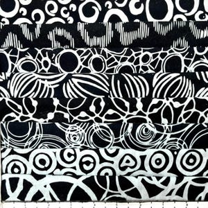 May include: A stack of fabric strips featuring various black and white patterns including circles, rings, and abstract lines. The fabric is layered horizontally, and a white ruler with black markings is visible at the bottom edge of the image.