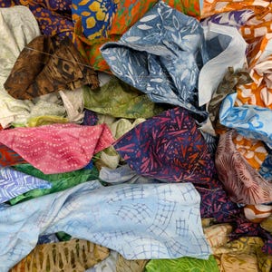 May include: A pile of colorful fabric scraps in various patterns and colors. The fabrics include shades of blue, orange, pink, green, and brown. Some fabrics have leaf and geometric designs.