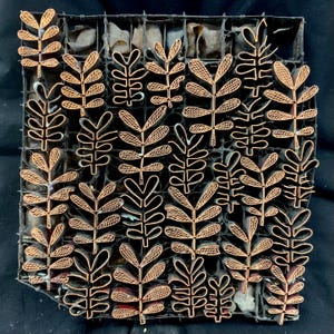 May include: A copper-colored leaf pattern stamp, featuring a grid of leaf designs. The leaves have detailed veins and are set against a dark background. The stamp is likely used for textile or paper printing.