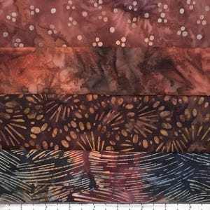 May include: A stack of fabric pieces in shades of brown, burgundy, and navy. The top piece has white polka dots, while the others feature abstract patterns. The fabrics appear to be batik or hand-dyed, suitable for quilting or crafting projects.