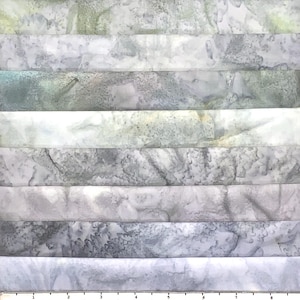 May include: A stack of fabric pieces in various shades of gray, white, and green. The fabric has a marbled or batik-like pattern, with subtle variations in color and texture. The fabric is arranged in horizontal stripes.