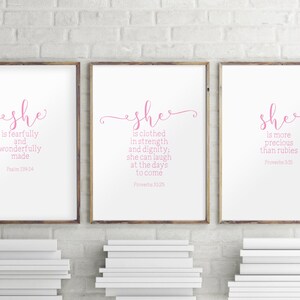 Peut inclure: Trois impressions encadr&eacute;es avec des fonds blancs et du texte rose. Le texte sur les impressions est "She is fearfully and wonderfully made Psalm 139:14", "She is clothed in strength and dignity: she can laugh at the days to come Proverbs 31:25", et "She is more precious than rubies Proverbs 3:15".