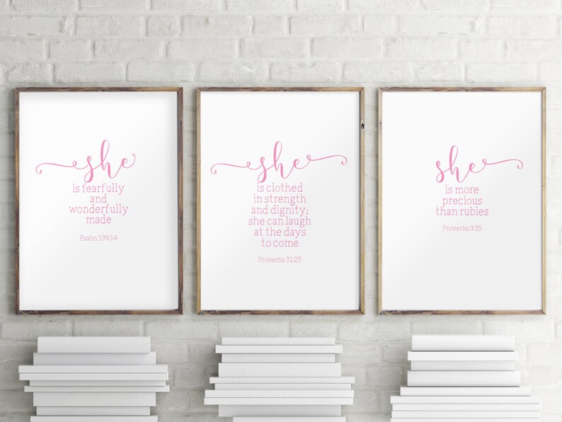Peut inclure: Trois impressions encadr&eacute;es avec des fonds blancs et du texte rose. Le texte sur les impressions est "She is fearfully and wonderfully made Psalm 139:14", "She is clothed in strength and dignity: she can laugh at the days to come Proverbs 31:25", et "She is more precious than rubies Proverbs 3:15".