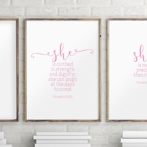 Peut inclure: Deux impressions encadr&eacute;es avec du texte rose sur fond blanc. L'impression de gauche pr&eacute;sente le texte "she is clothed in strength and dignity: she can laugh at the days to come Proverbs 31:25". L'impression de droite pr&eacute;sente le texte "sh is mo preci than r Proverb".