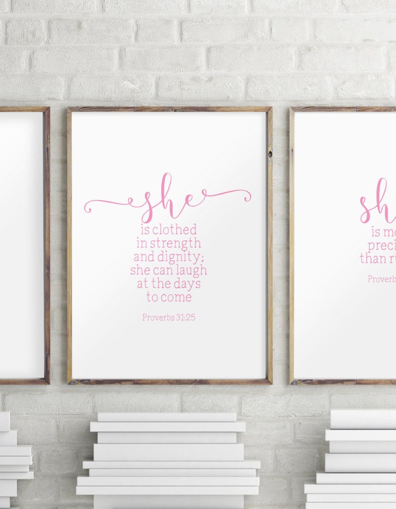 Peut inclure: Deux impressions encadr&eacute;es avec du texte rose sur fond blanc. L'impression de gauche pr&eacute;sente le texte "she is clothed in strength and dignity: she can laugh at the days to come Proverbs 31:25". L'impression de droite pr&eacute;sente le texte "sh is mo preci than r Proverb".