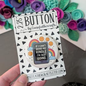 May include: A 2.25-inch button with the text "If I can't bring my Kindle I'm not going" on a white background. The button features a rainbow, smiley faces, and a Kindle graphic. The button is on a black and white patterned card.