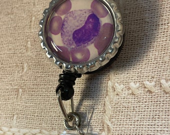 May include: A silver retractable badge holder with a purple bead charm. The badge holder features a round, clear, plastic cover with a purple and white image of a cell.