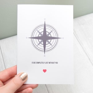 May include: A white card with a grey compass design and the text "I'd be completely lost without you". A small red heart is below the text.