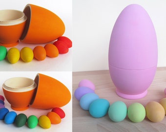 May include: Two sets of wooden nesting eggs. One set is orange and the other is light purple. Each set includes a larger egg that opens to reveal a smaller egg inside. Both sets include a rainbow of smaller eggs that fit inside the larger egg.