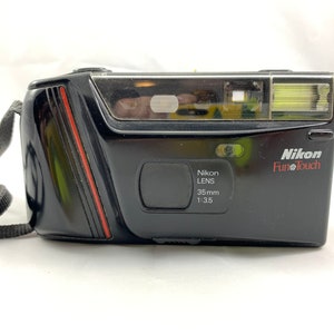 Pode incluir: Uma câmera Nikon FunTouch 35 mm preta com uma faixa vermelha na lateral. A câmera tem uma alça preta.