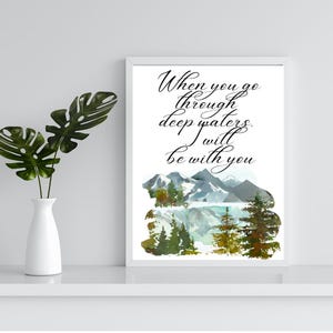 May include: A white framed print with a watercolor illustration of mountains and a lake. The text "When you go through deep waters, I will be with you" is written in black cursive.