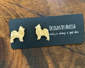 May include: A pair of gold-colored dog silhouette earrings. The earrings are on a black card with the text "Designs by Anissa Jewelry is always a good idea".