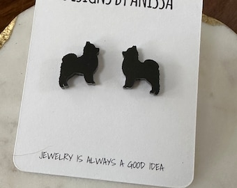 May include: A pair of black stud earrings featuring a silhouette of a dog. The earrings are displayed on a white card with the text "DESIGNS BY ANISSA" and "JEWELRY IS ALWAYS A GOOD IDEA".