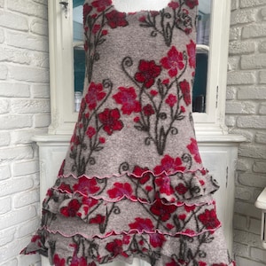 Peut inclure: Robe sans manches grise avec un motif floral dans les tons de rouge et de rose. La robe présente un ourlet à volants et est présentée sur un mannequin. Le motif floral comprend des tiges et des feuilles marron foncé.