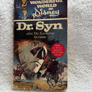 May include: A vintage paperback book titled "Dr. Syn" from "The Wonderful World of Disney" series. The cover features a scarecrow-like figure and a rider on horseback. The book has a price tag of $1.25.