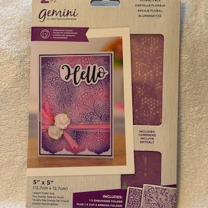 May include: A Gemini embossing folder set with a floral lace design. The package includes a 5" x 5" (12.7cm x 12.7cm) embossing folder and a cut & emboss folder. The card features the word "Hello" and decorative flowers.