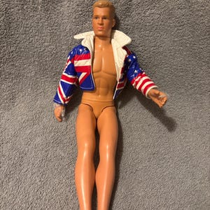 May include: A nude male action figure wearing a blue, white, and red jacket with stars and stripes. The jacket has a white fur collar.