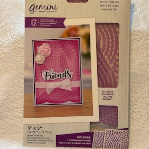 May include: A set of two 5-inch by 5-inch (12.7 cm x 12.7 cm) embossing folders for crafting. The folders feature a cable knit design in purple and include one embossing folder and one cut and emboss folder. The image shows a sample card with the words "Friends" embossed on it.