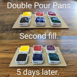May include: A close-up of watercolour paint pans in various colours, including yellow, red, purple, and green, arranged on a cardboard surface. The text "Double Pour Pans" and "Second fill" are visible. The bottom row of pans is labeled "5 days later."