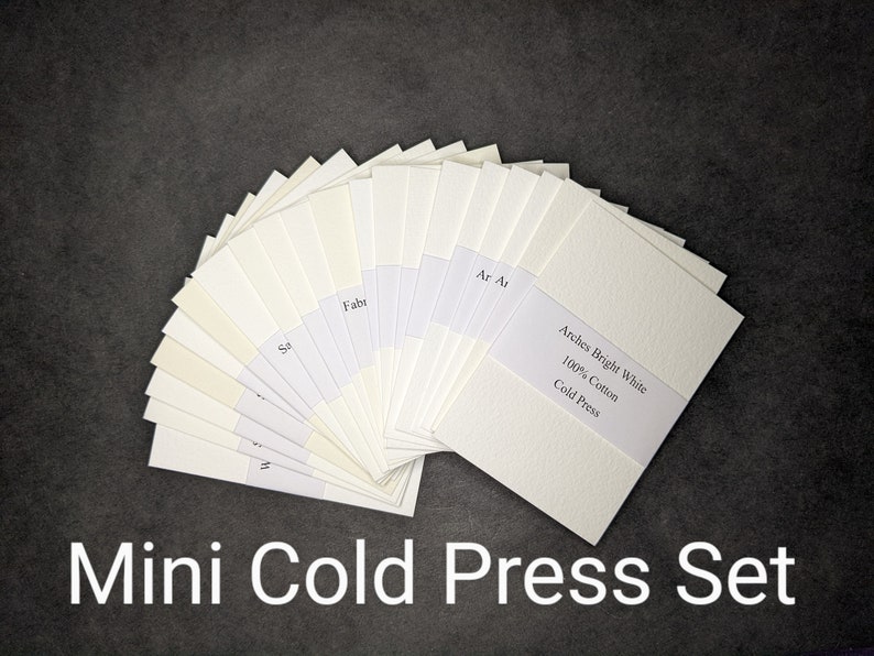 Puede incluir: Un abanico de muestras de papel de prensa en fr&iacute;o blanquecino, etiquetadas. El conjunto incluye papel Arches Bright White 100% Cotton Cold Press. Las palabras "Mini Cold Press Set" est&aacute;n en la parte inferior de la imagen.
